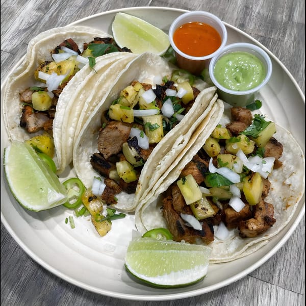 Three La Fonda St al pastor tacos with pineapple, onions, cilantro, lime, and two sauces.